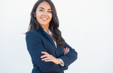 Smiling confident businesswoman posing with arms folded. Happy beautiful black haired young Latin woman in formal suit standing for camera over white studio background. Corporate portrait concept